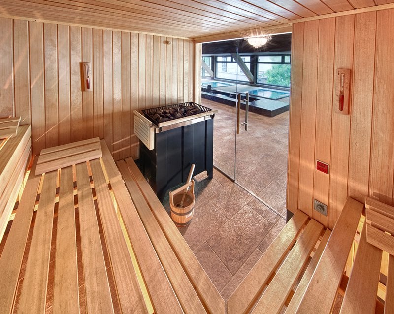 Drevená hotelová sauna s tlmeným osvetlením a sklenenou stenou.