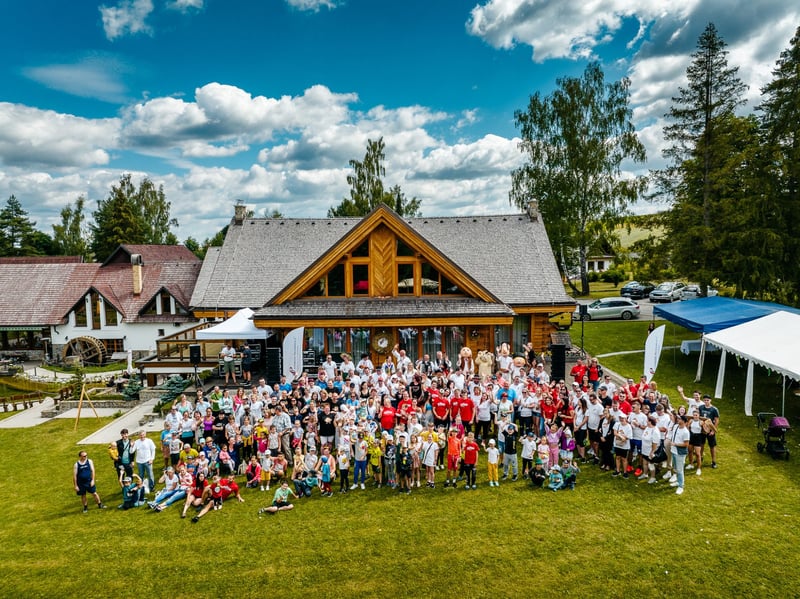 Letecká skupinová fotka zamestnancov a ich rodín pred drevenou chatou počas firemného family day v prírode